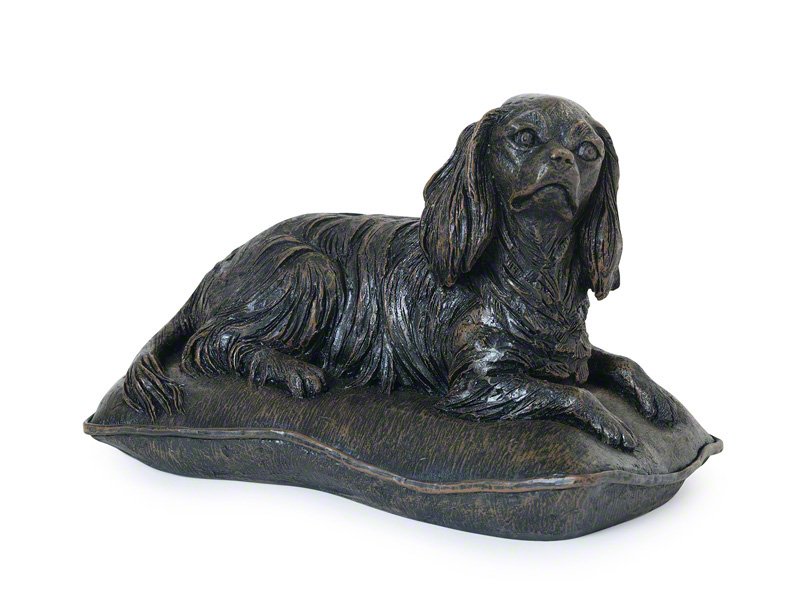A detailed cast resin Cavalier King Charles Spaniel figurine urn with a bronze finish reclining on a soft pillow, showcasing intricate fur textures and a lifelike posture.