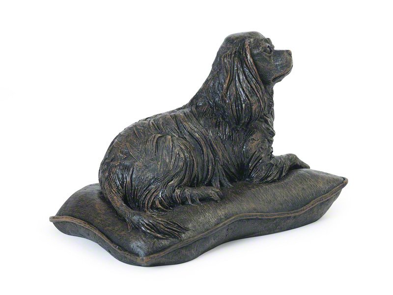 A detailed cast resin Cavalier King Charles Spaniel figurine urn with a bronze finish reclining on a soft pillow, showcasing intricate fur textures and a lifelike posture.