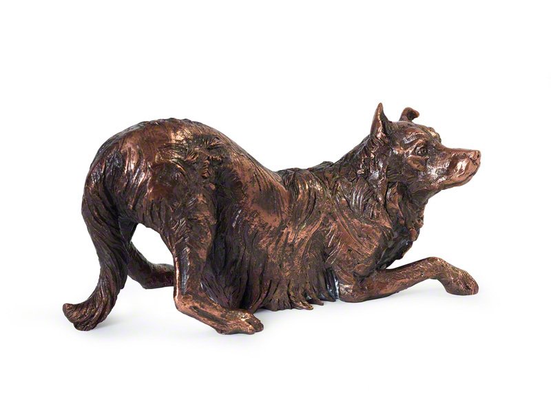 A detailed copper plated sculpture of a Border Collie lying down, featuring a textured coat and a curious expression.