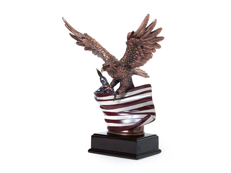 A bronze eagle sculpture perched atop a waving American flag, mounted on a black base, symbolizing freedom and patriotism.
