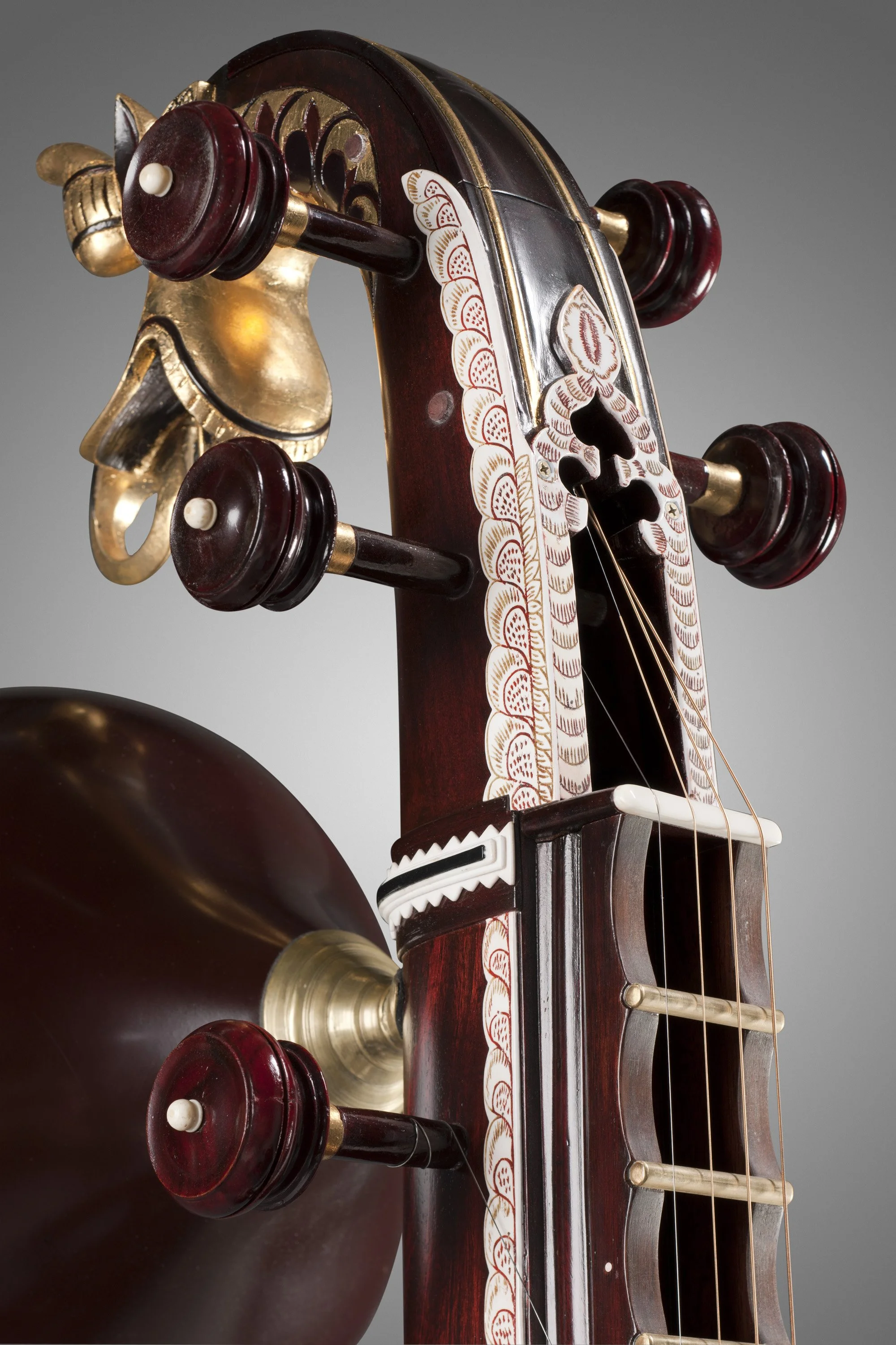 Close-up of a veena's headstock with tuning pegs and ornate design.