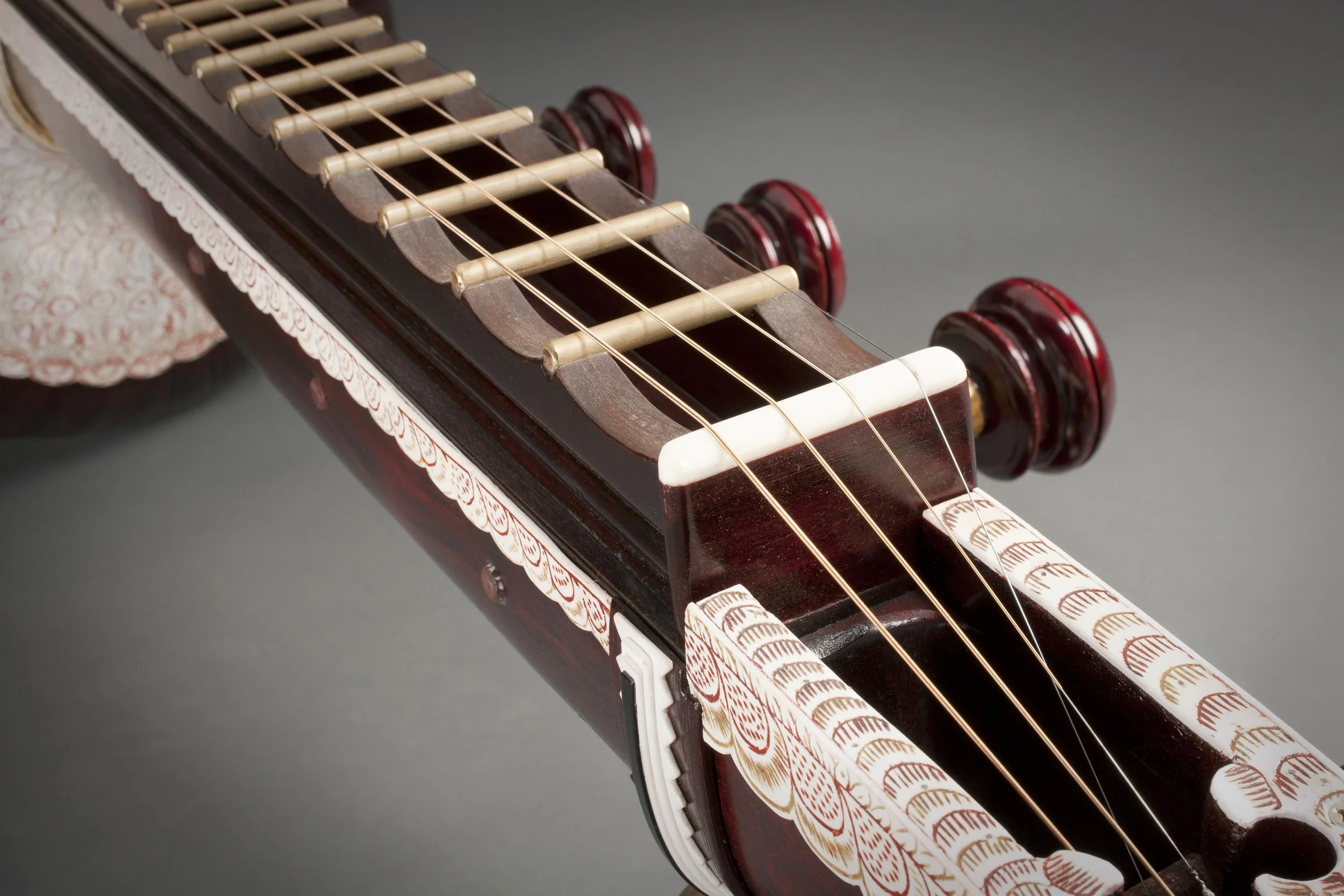 Close-up of a sitar's strings and bridge, featuring ornate carvings and tuning pegs.