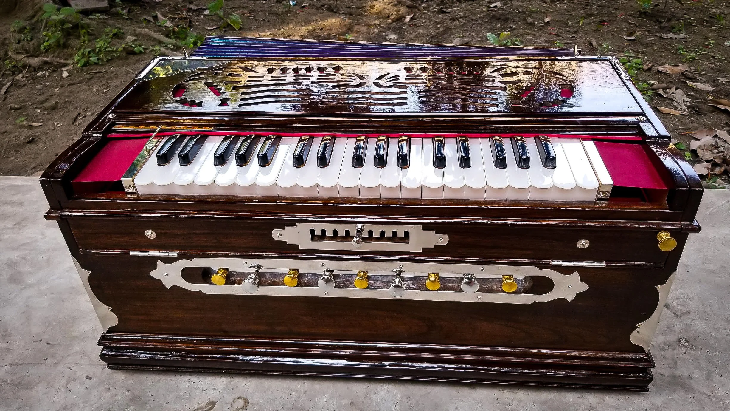 Brown wooden harmonium with white and black keys on a concrete surface.