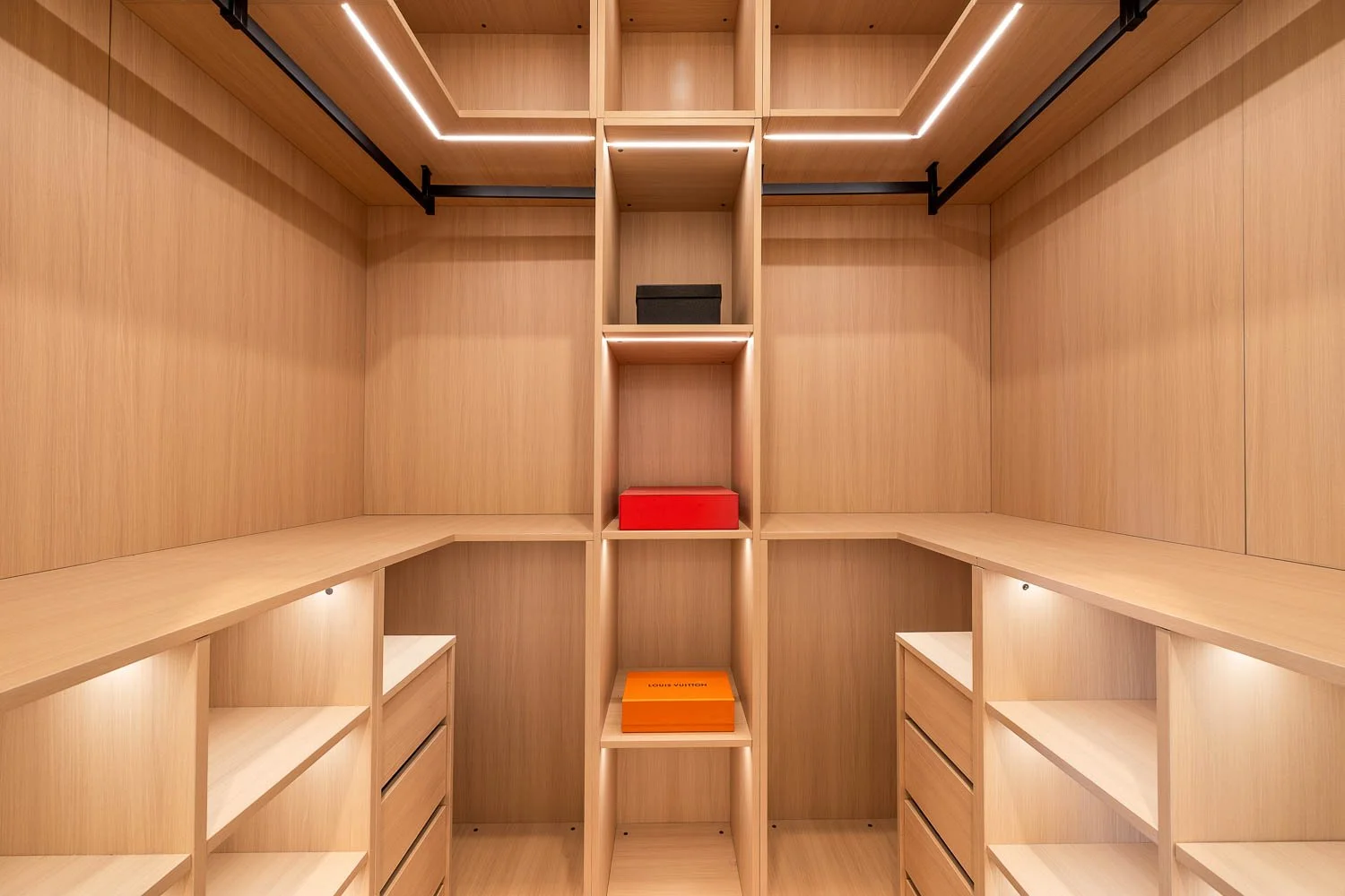 An empty, modern walk-in closet with wooden shelves, drawers, and ceiling lighting, featuring a few boxes on the central shelves