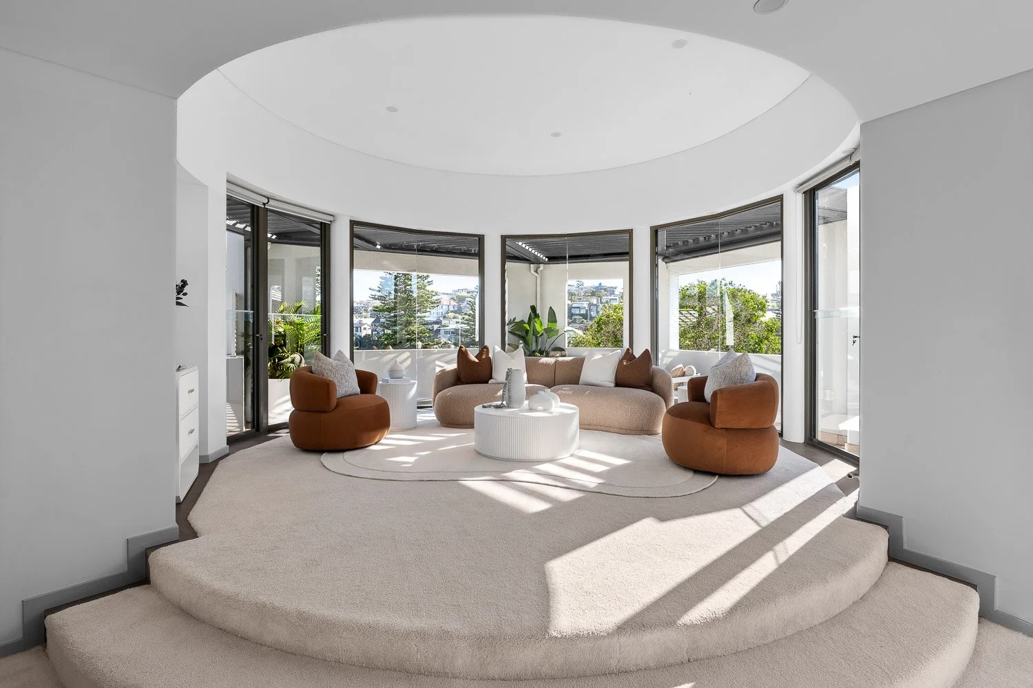 Modern living room with a curved bay window, beige and brown furniture, and natural light.