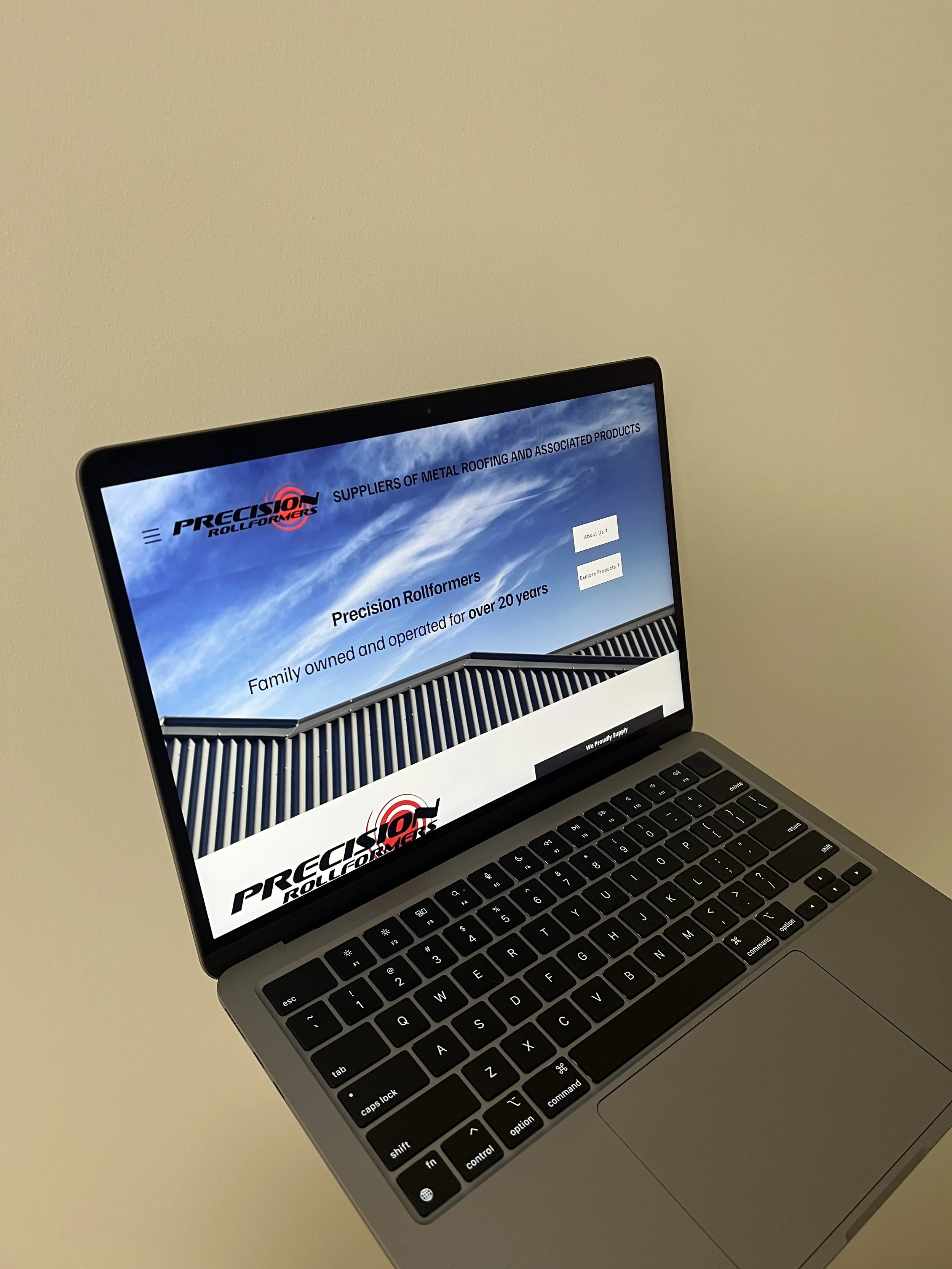Laptop displaying a website for Precision Rollformers, suppliers of metal roofing products, featuring their logo and text about their over 20 years of family ownership.