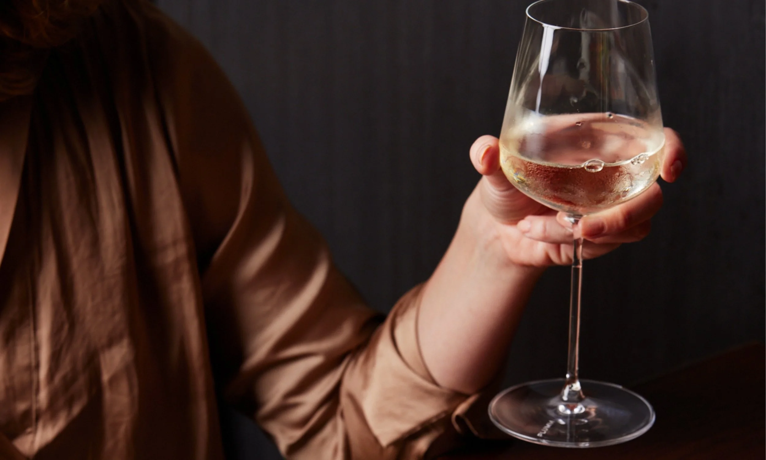 A woman holding a glass of white wine.