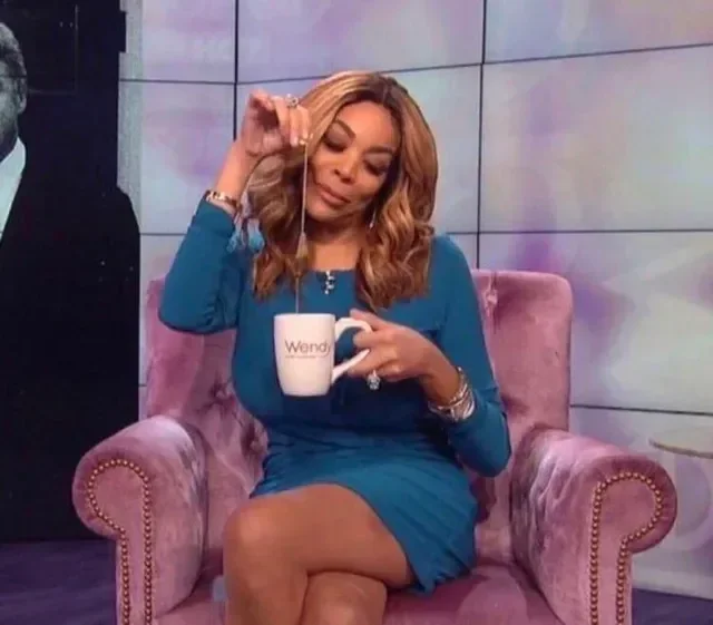 image of a black woman sitting cross-legged and lifting a tea bag out of a mug. she sits in a pink floor with her legs crossed.