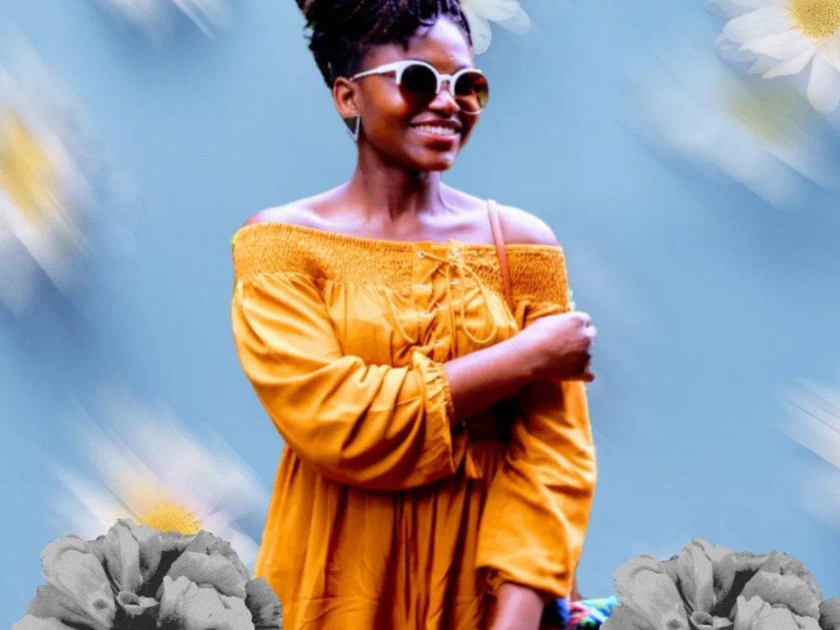 A black person in an orange dress smiles in front of a blurry blue background with daisies.