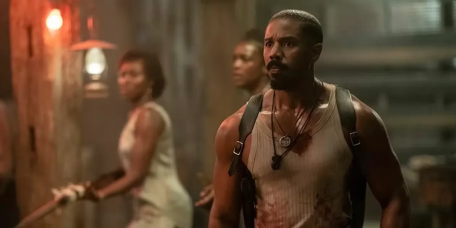 still from the film sinners, showing michael b jordan facing forward expectatntly while two women stand near him in the background