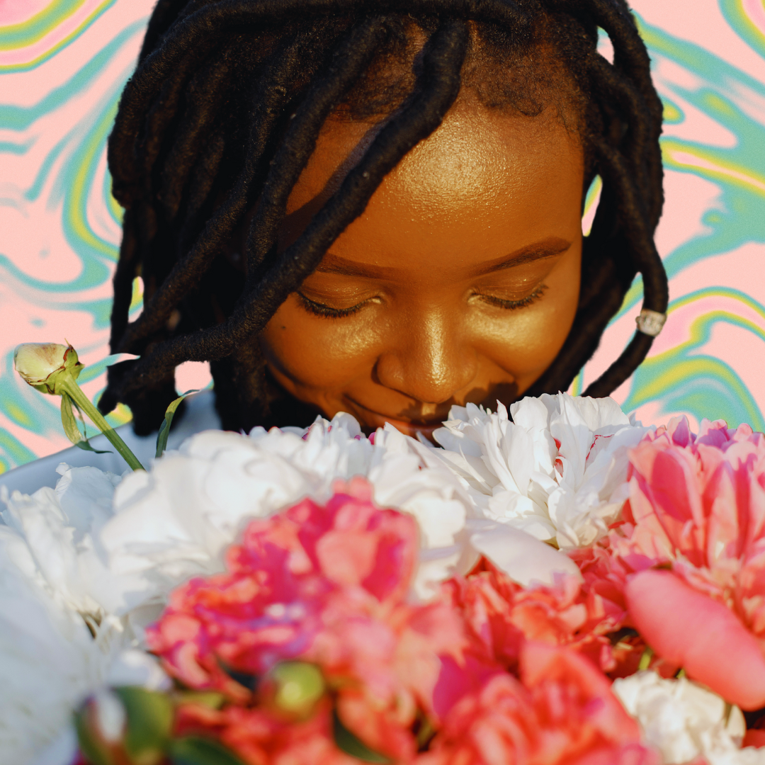 A Black person looks down and smiles at a bouquet of pink and white flowers. They are pictured in front of a marbled blue, yellow, and light pink background.