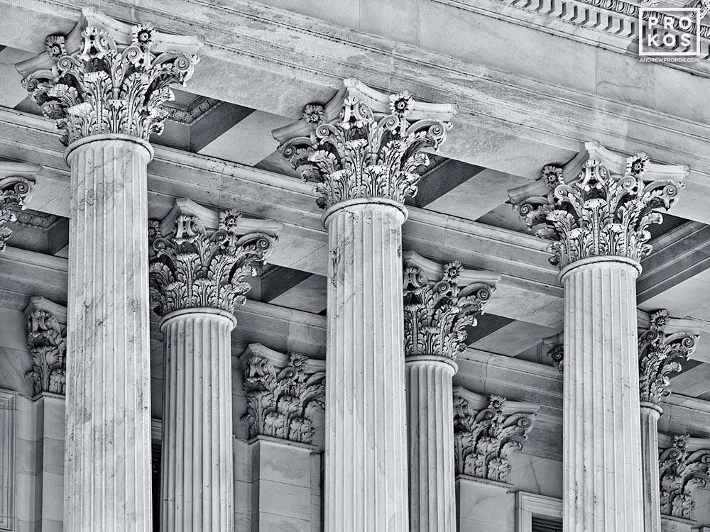 A close-up view of tall Corinthian columns with ornate capitals featuring acanthus leaves and scrolls, part of a neoclassical building facade in black and white.