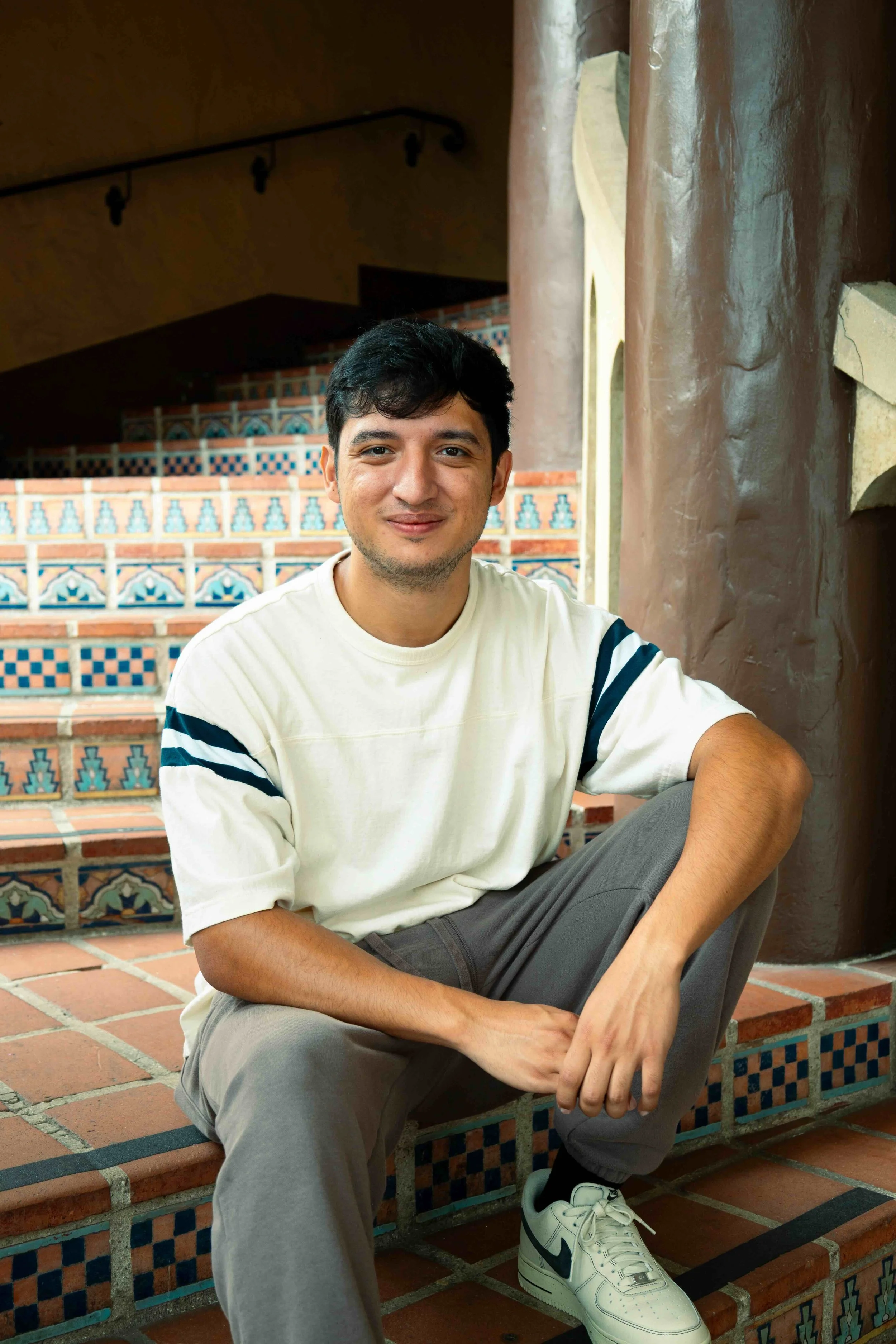 Cinematographer Angel Gutierrez sitting on colorful tiled stairs inside a building with earthy tones and arched window openings.