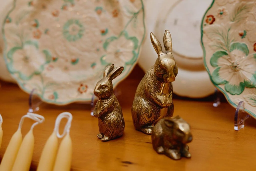 Three metallic rabbit figurines of different sizes among decorative plates with floral patterns.