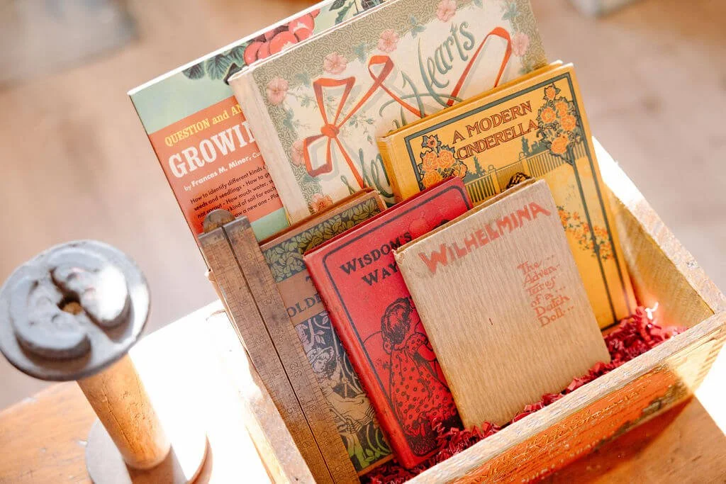 A wooden box filled with illustrated vintage-style books and a candle on a wooden table.