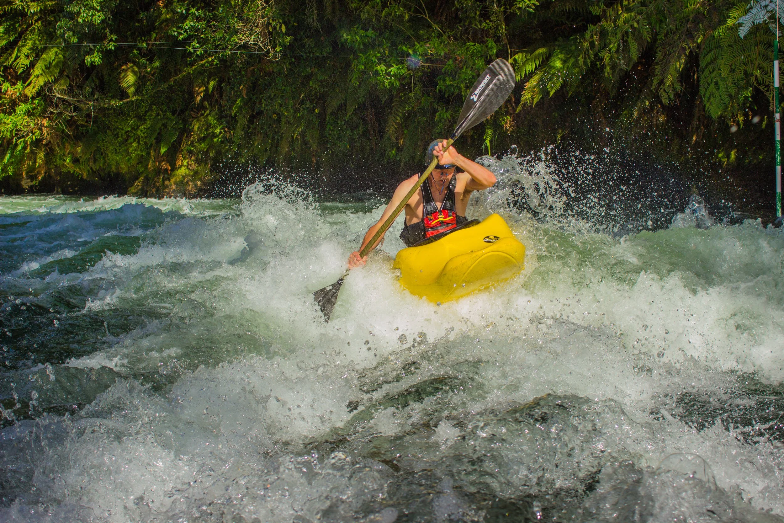 Person kayaking in turbulent river with lush green foliage in the background.
