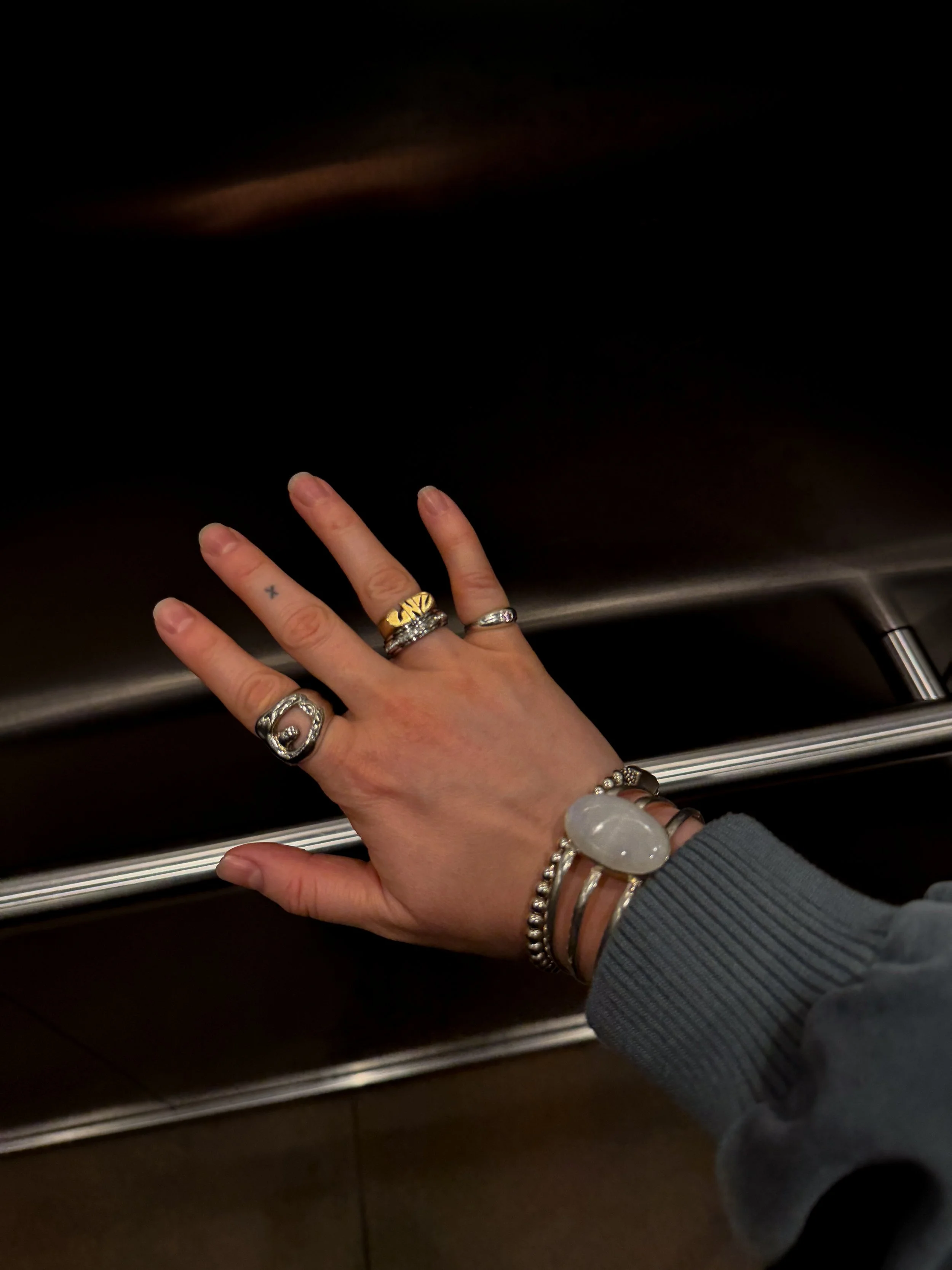 Close-up of a hand wearing multiple rings and bracelets resting on a dark wooden surface.
