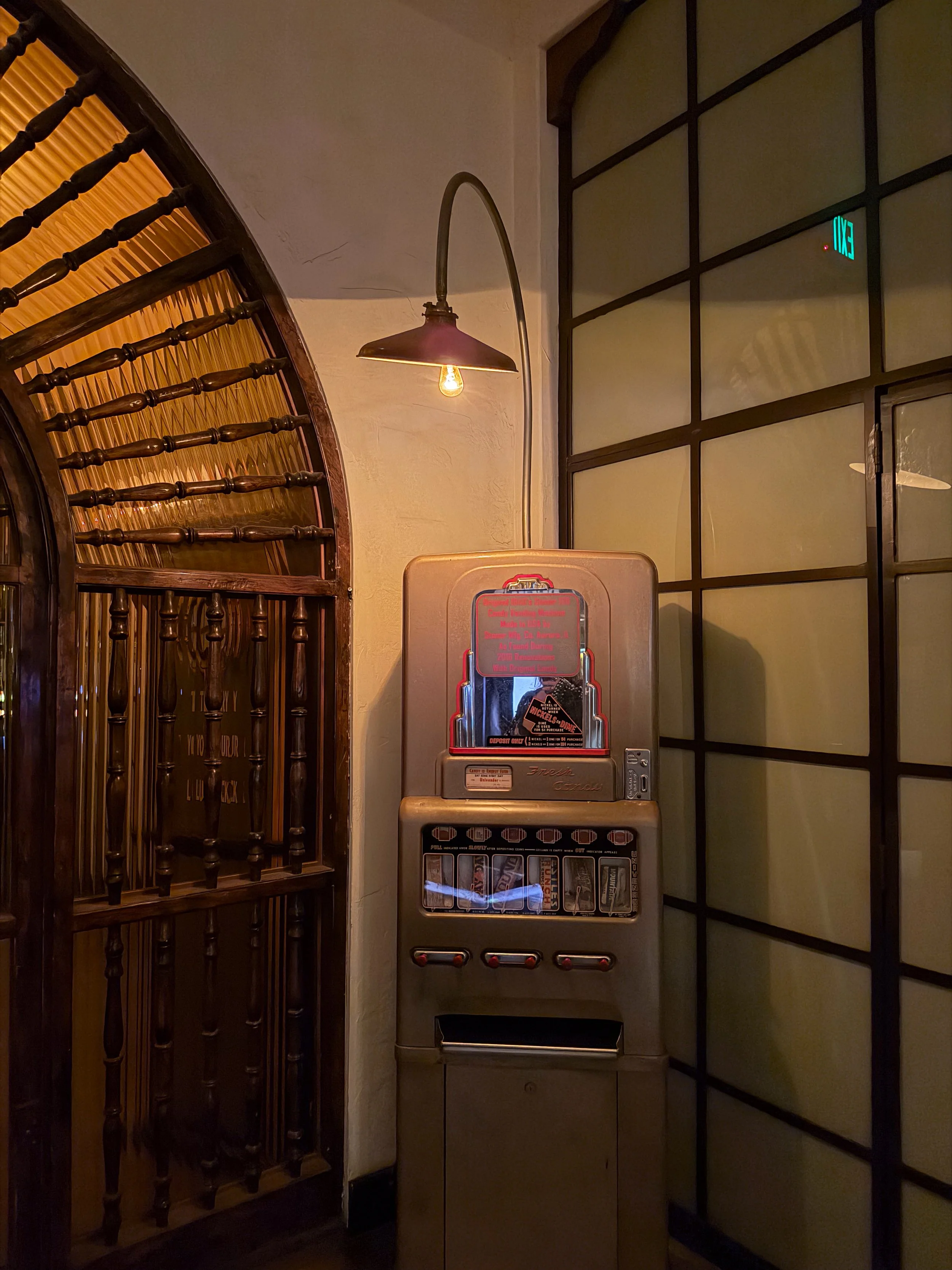 Vintage candy vending machine beside a wooden staircase and hanging lamp in a dimly lit interior