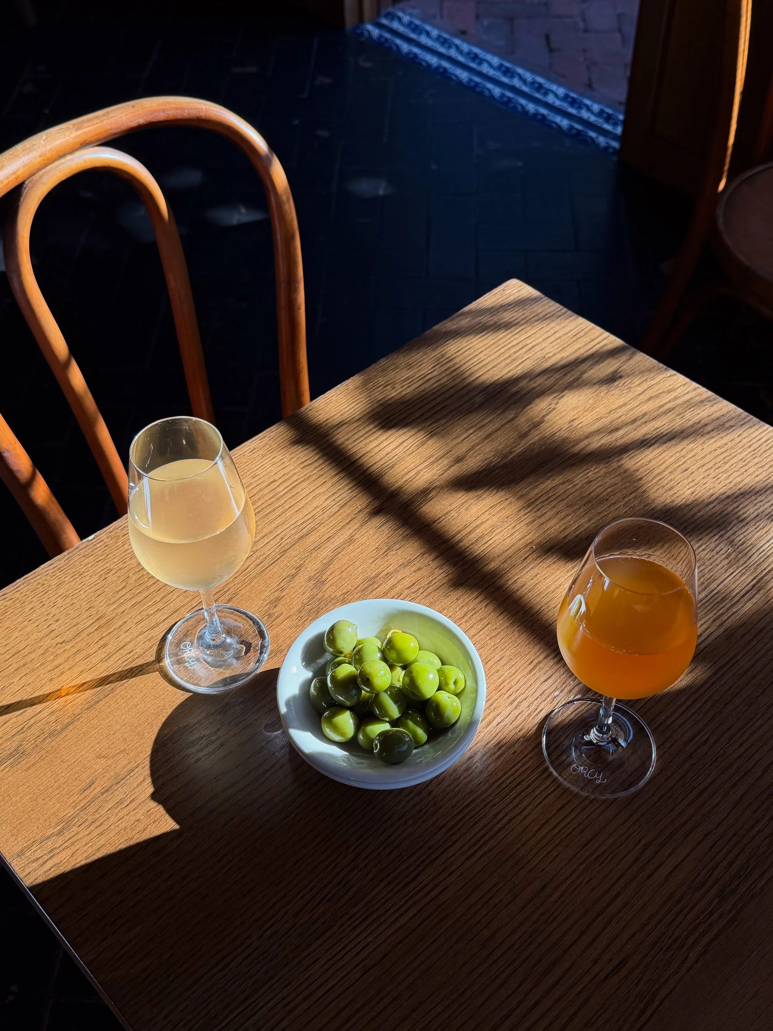 Wooden restaurant table with two cocktails and a bowl of green olives