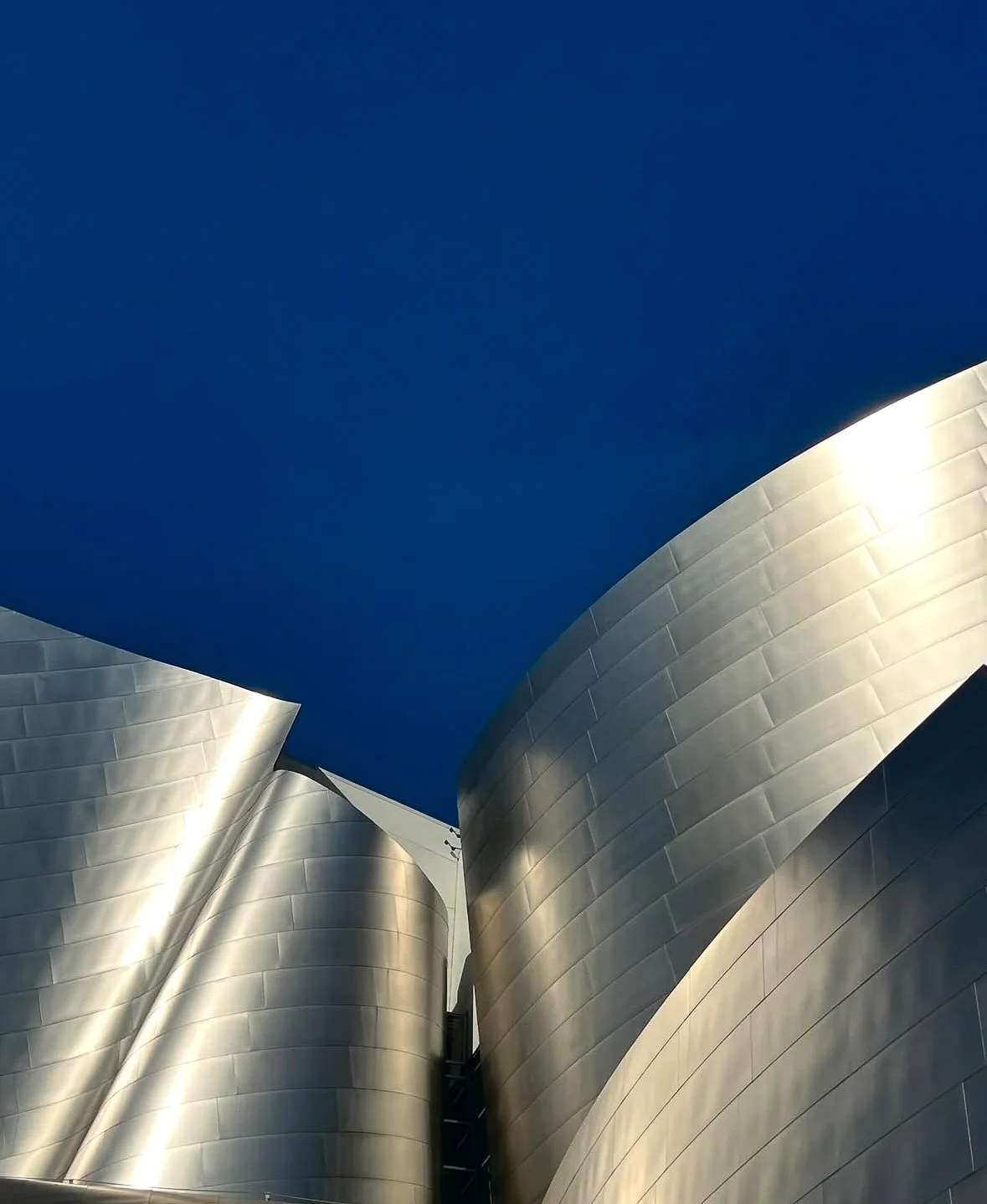 Abstract view of the Walt Disney Concert Hall’s curved stainless steel exterior against a deep blue sky