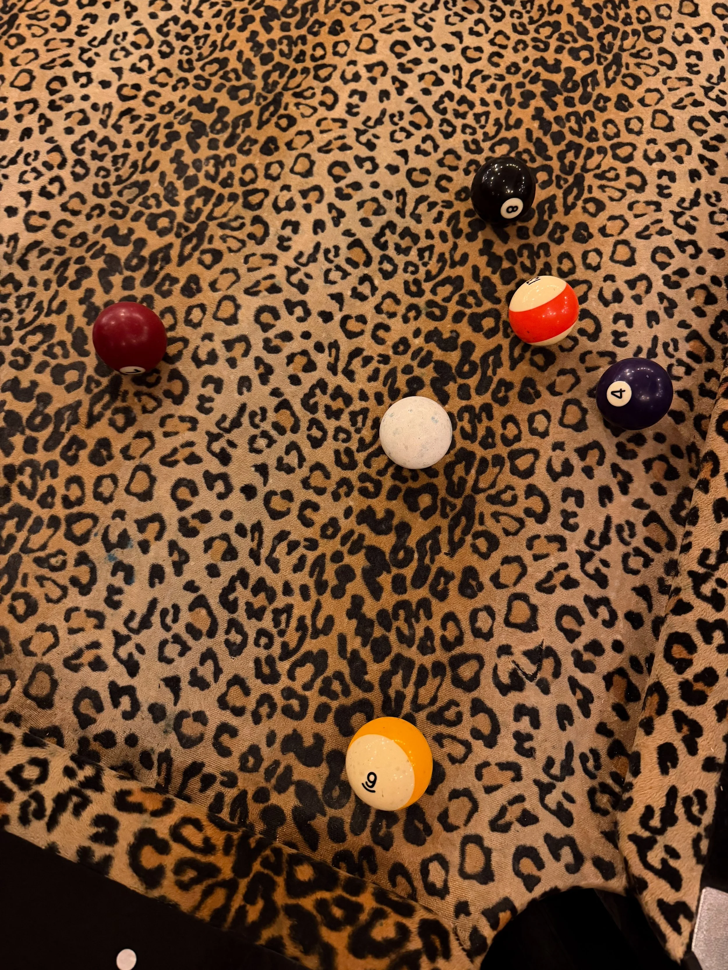 Several billiard balls scattered across a leopard-print pool table, including numbered balls 8, 4, 6, and 9.