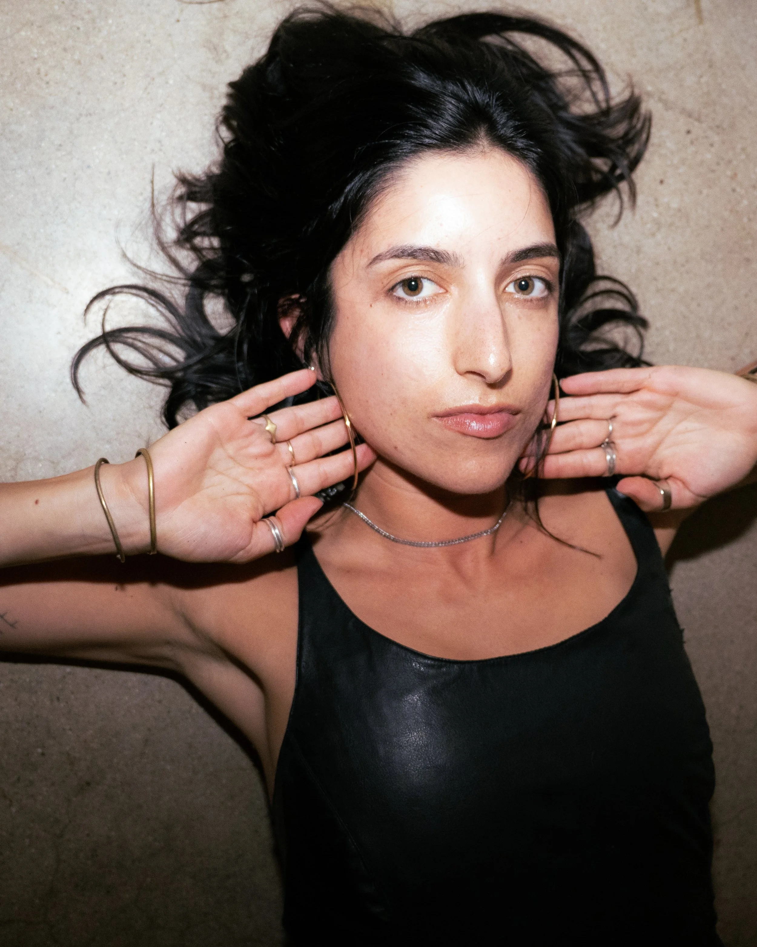 Close-up portrait of a woman with dark hair, brown eyes, and jewelry posing with her hands near her face.