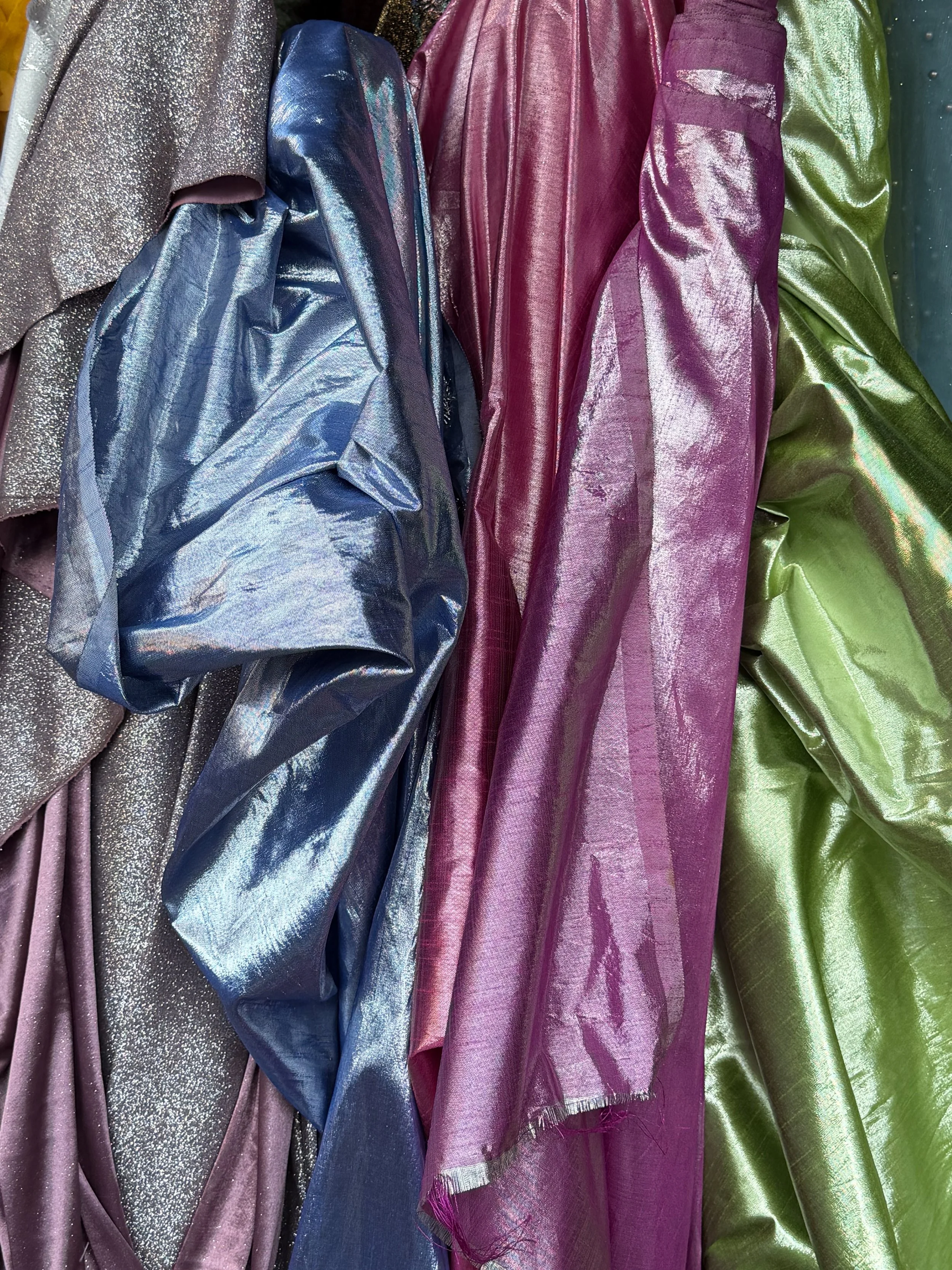 Close-up of colorful shimmering fabrics in silver, navy blue, burgundy, purple, and green.