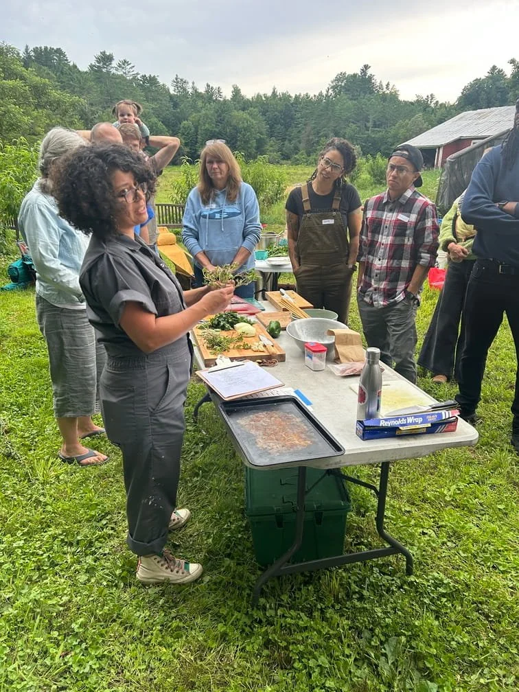 chef with herbs in hand at table with cooking ingredients surrounded by interested group