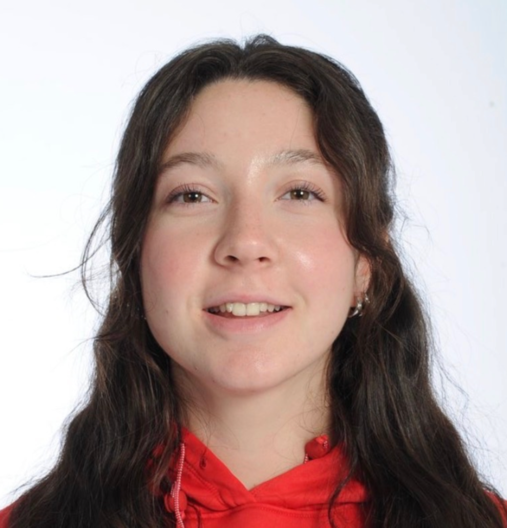 A young woman with long wavy brown hair wearing a red hoodie and smiling at the camera against a plain white background.