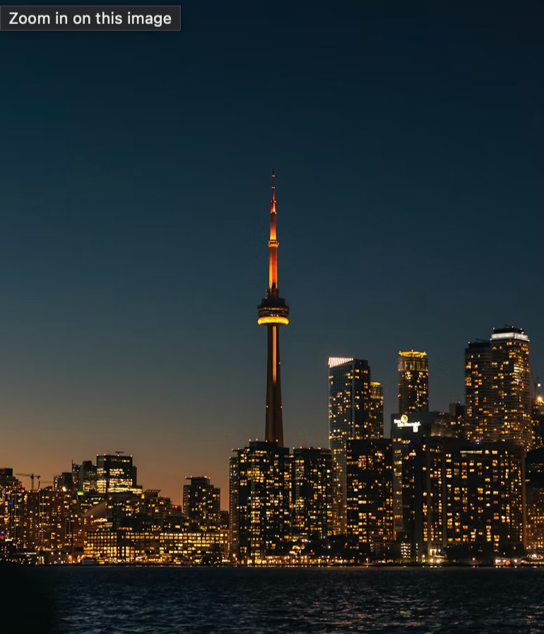 Nighttime city skyline of Toronto with illuminated skyscrapers and the CN Tower, reflected on the water.