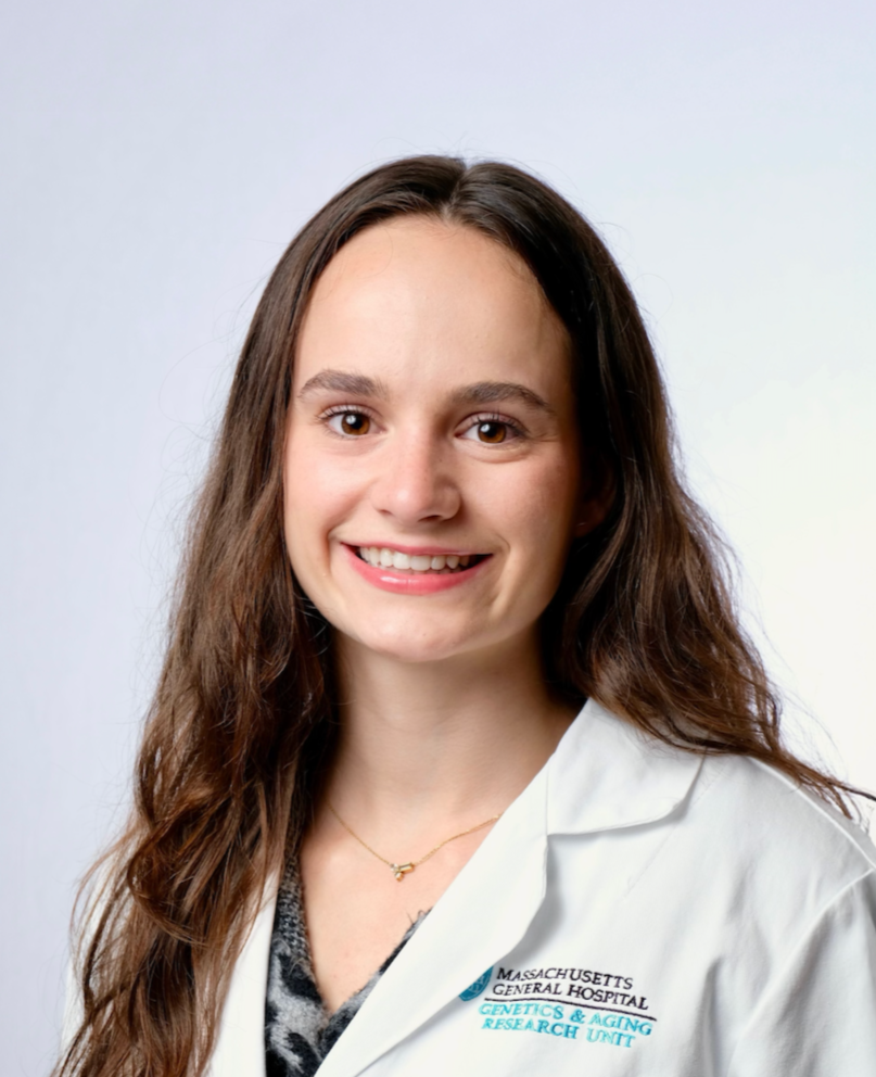 Madeline Wilkin - A young woman wearing a white lab coat with the logo of Massachusetts General Hospital and the Genetics & Aging Research Unit, smiling against a neutral background.