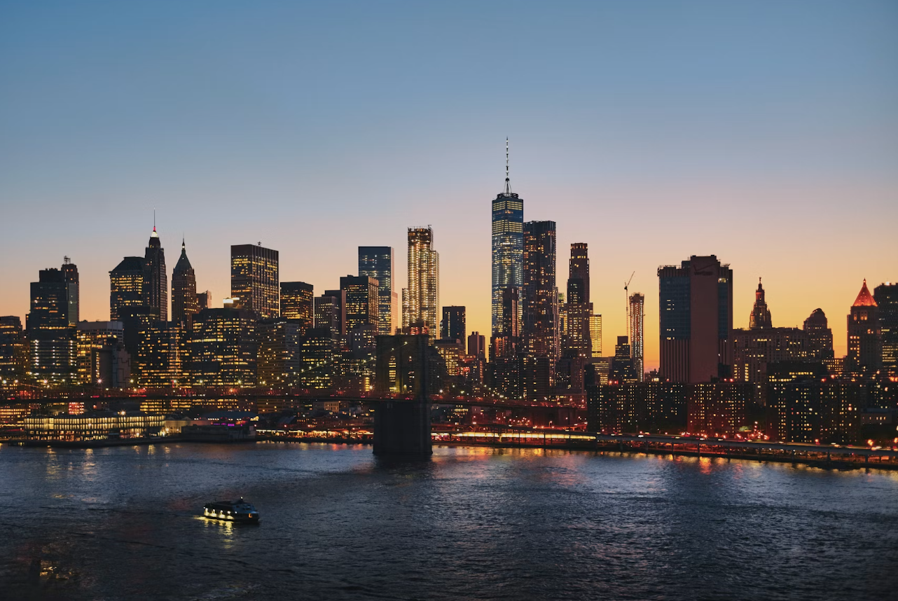 City skyline of New York City with One World Trade Center, reflected in the water at sunrise or sunset.