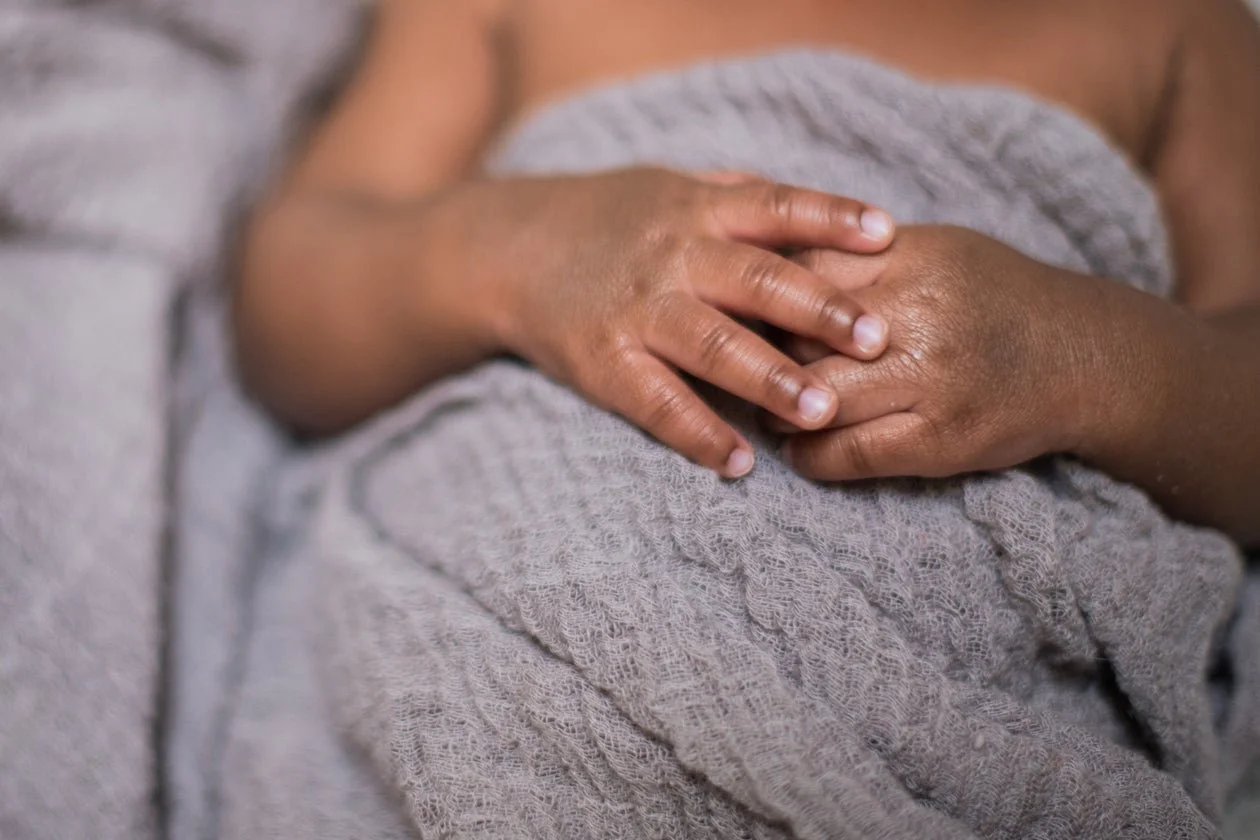 Close-up of a baby's hand resting on a blanket.