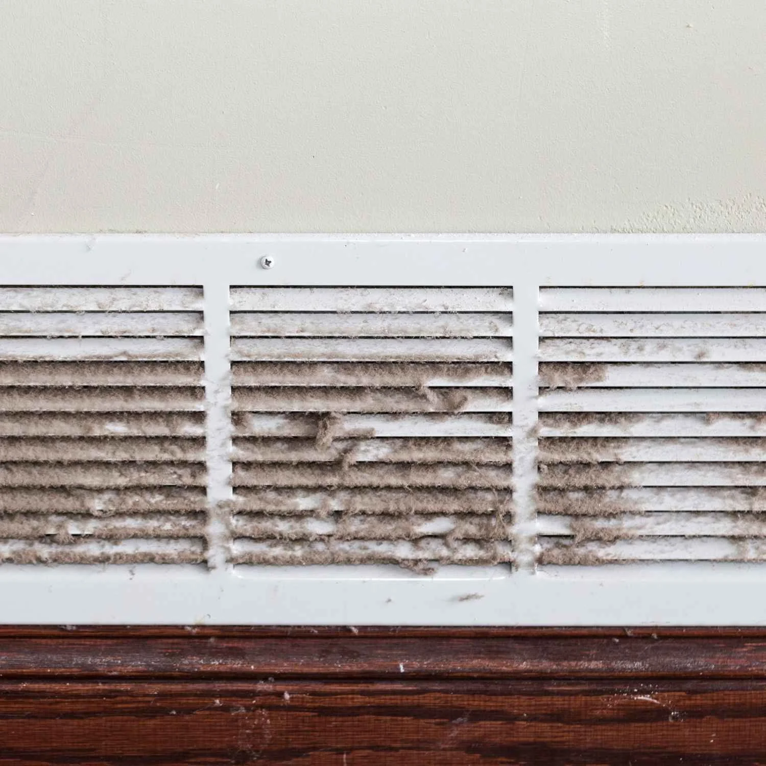 Dusty air vent on wall with wooden baseboard