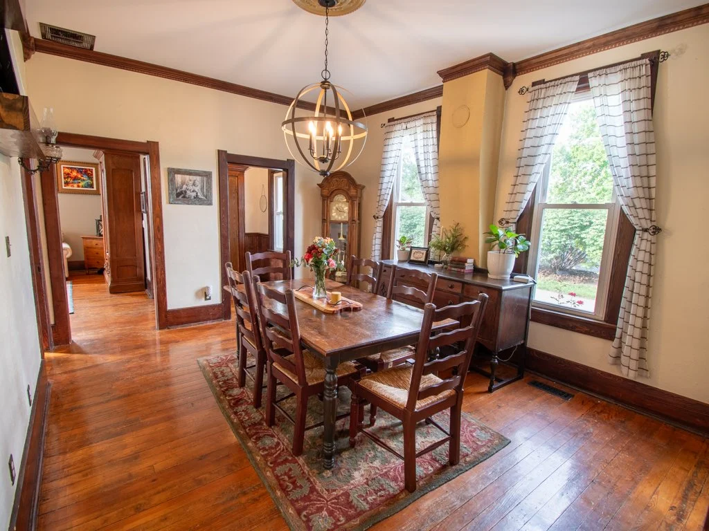 Dining room with wooden table, eight chairs, a sideboard, decorative curtains, and a chandelier