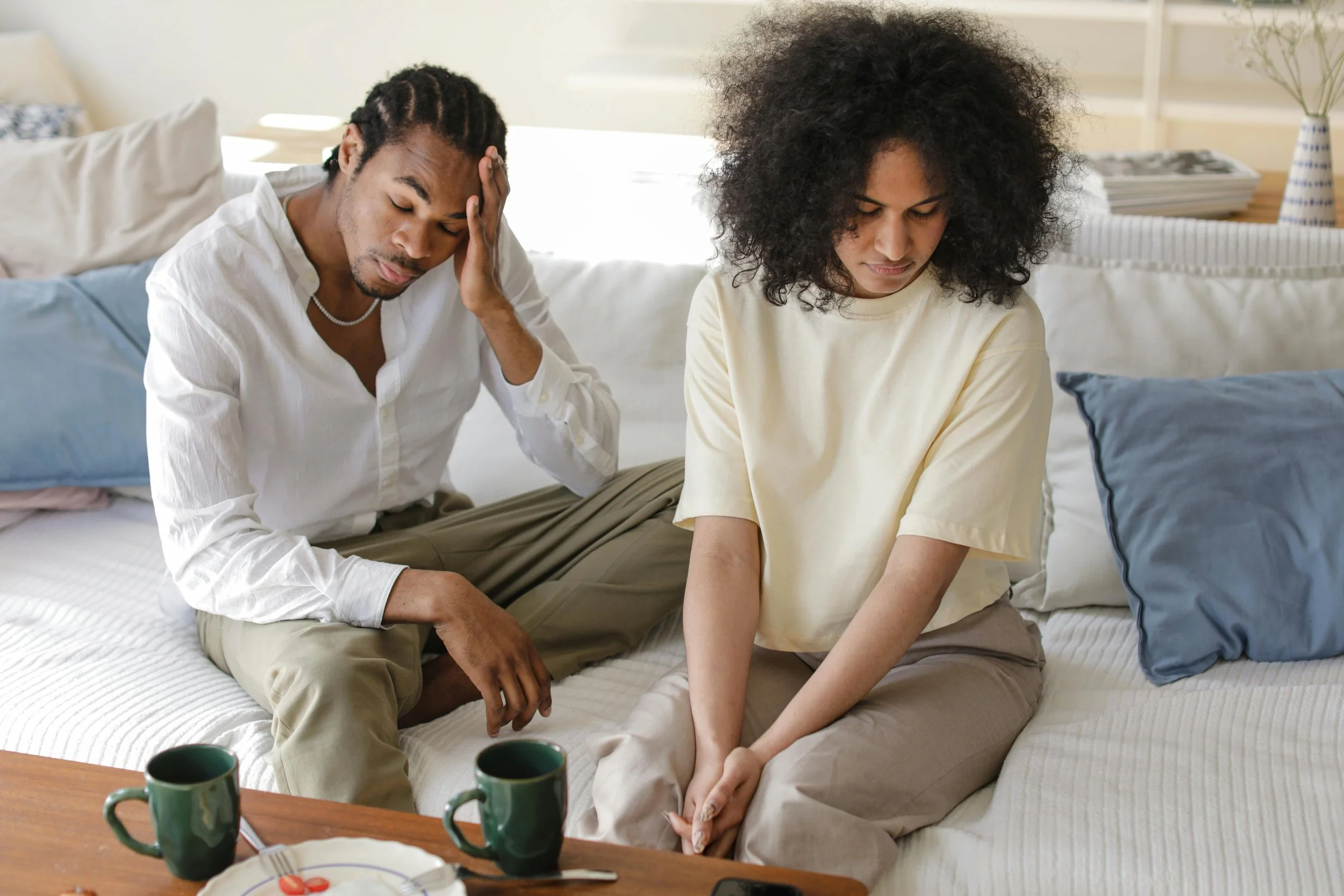 A stressed man and a solemn woman sitting on a couch, representing emotional distance and exhaustion in a relationship.