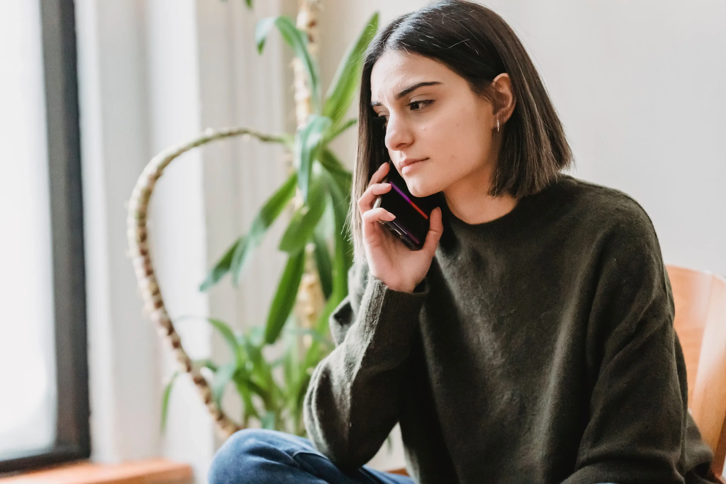 A thoughtful woman engaged in a phone conversation, representing someone taking the first step to schedule a therapy consultation call.