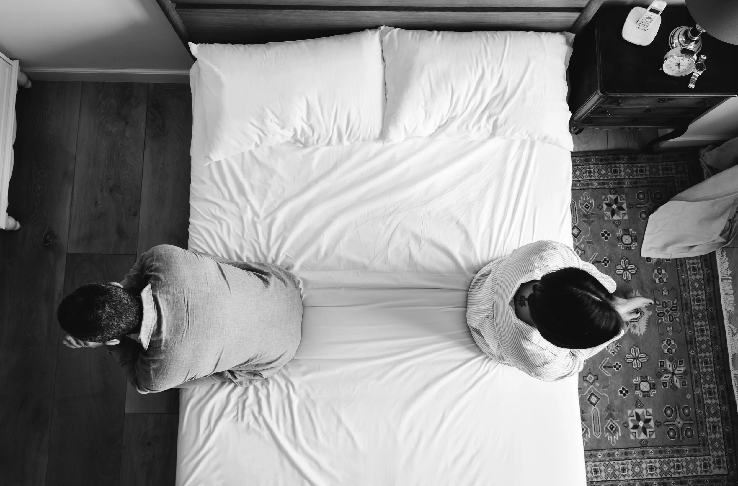 A couple sitting on opposite edges of a bed with their backs turned to each other, illustrating the emotional distance and loss of safety following a betrayal.