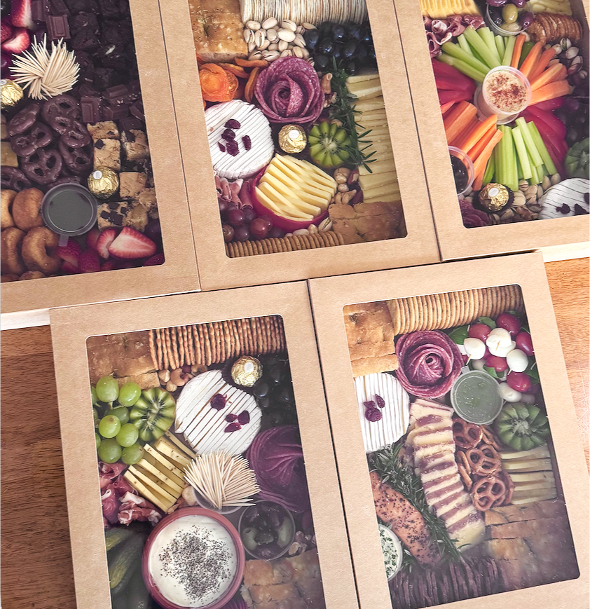 Assorted snack platter featuring cheeses, strawberries, blueberries, raspberries, chocolate wrapped candies, crackers, olives, sliced vegetables, dips, and assorted meats.
