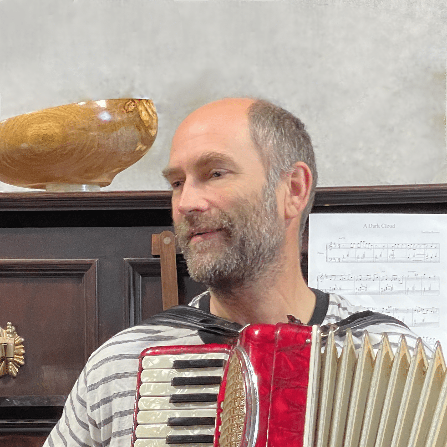 Lachlan Brown playing a red accordion, with a piano and sheet music in the background.