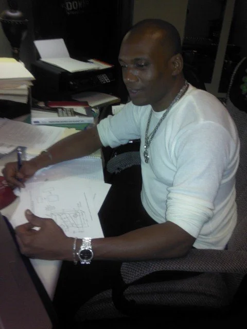 Person in a white shirt sitting at a desk, holding a pen, with documents and a binder on the desk.