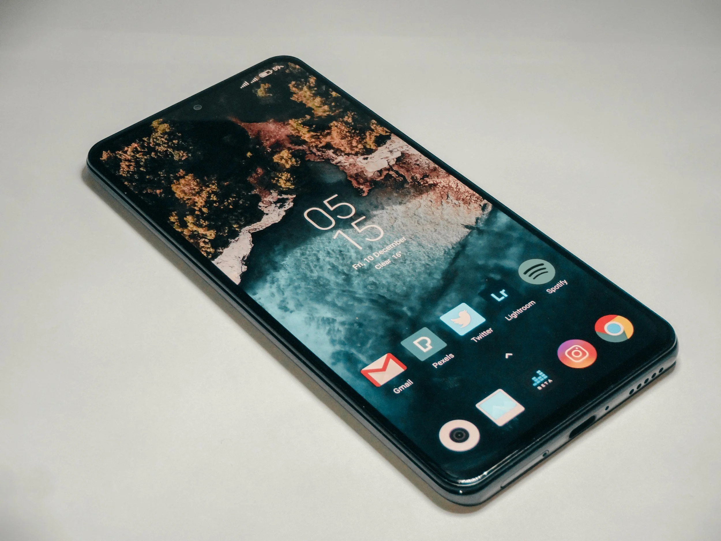 Modern smartphone facing up on a white surface, showing a colorful nature wallpaper and app icons on the screen.
