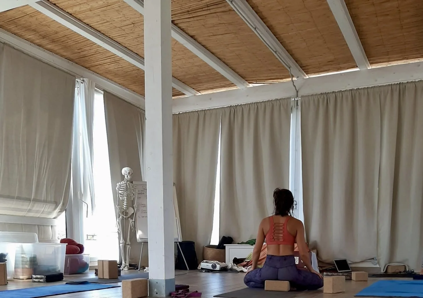 Eine Frau macht Yoga in einem Raum mit langen Vorhängen, einem menschlichen Skelett und Yoga-Zubehör.