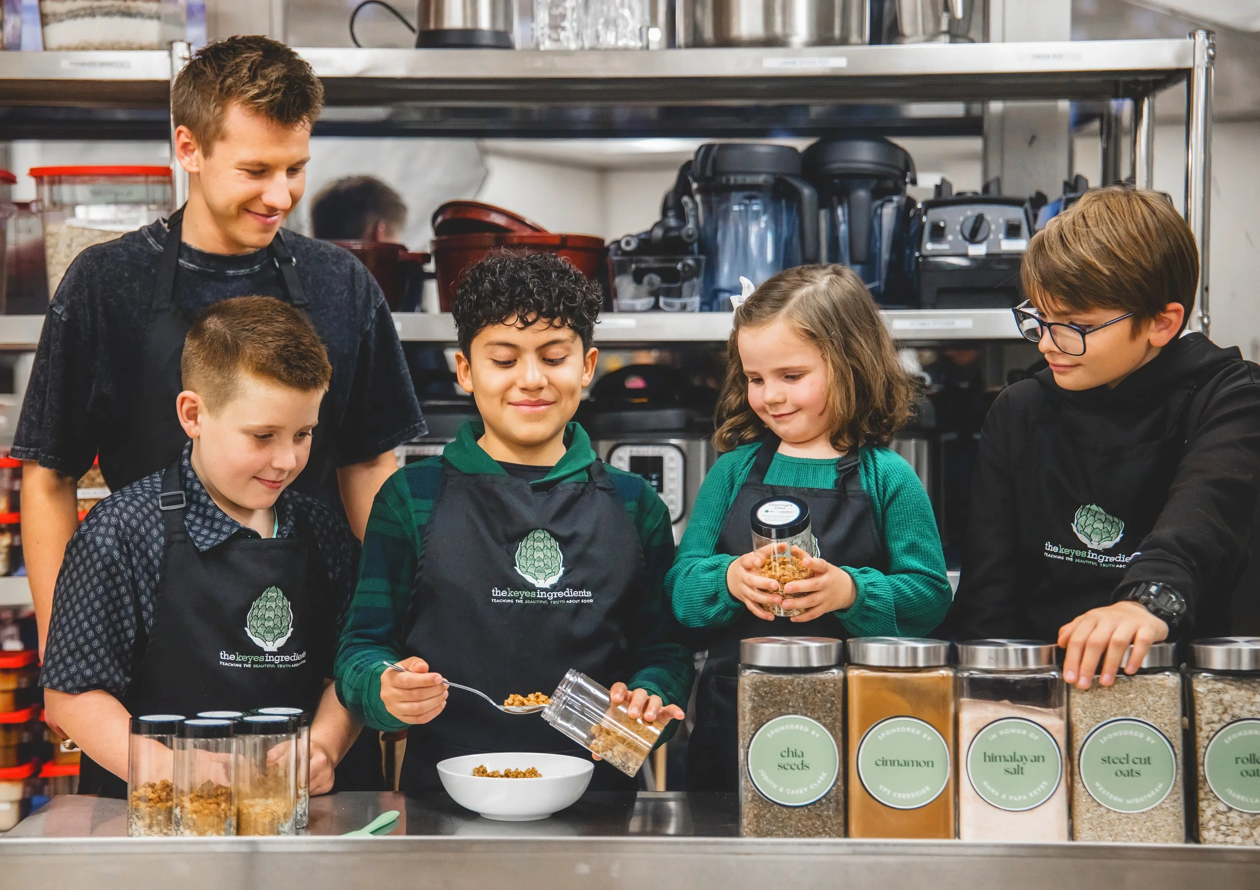 Group of children and an adult cooking with various spices in jars in a kitchen or classroom setting.