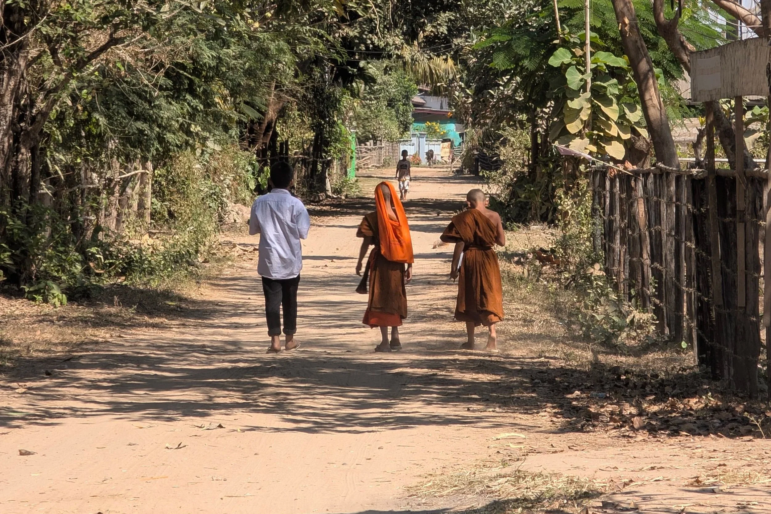 Quête matinale des moines bouddhistes marchant paisiblement dans un village laotien.
