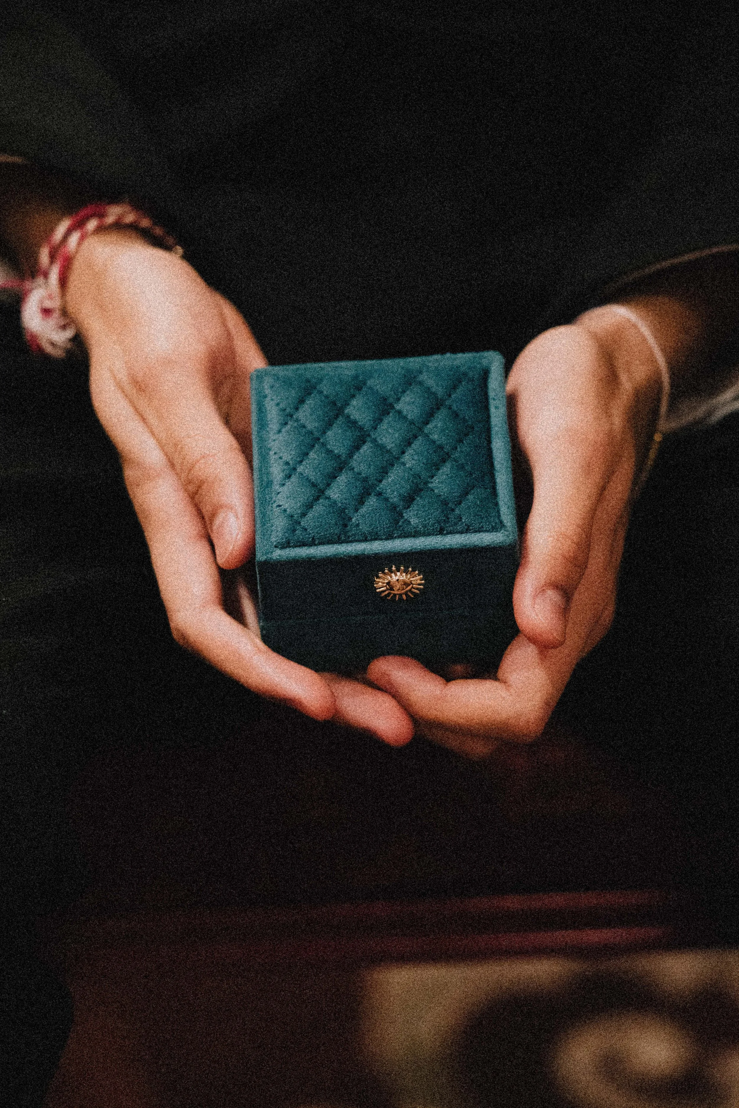 Person holding a small velvet jewelry box with a quilted pattern and a gold sun-shaped clasp. Weddings in london