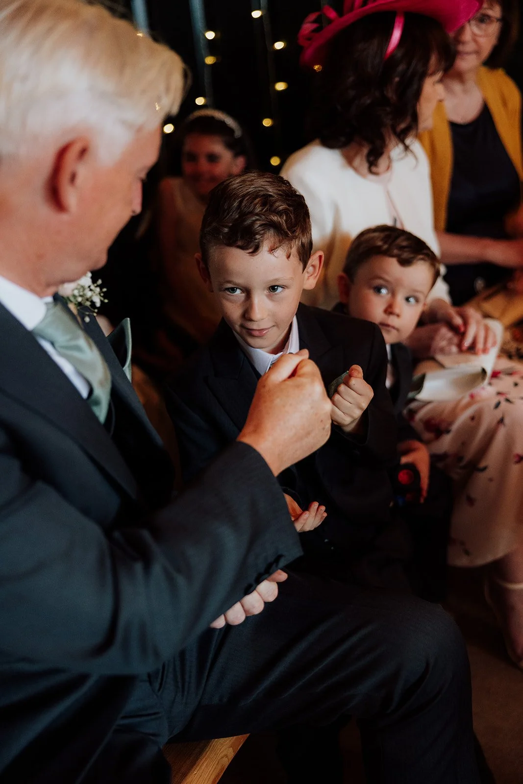 peckforton castle weddings, documentary wedding photographer based in cheshire. boy and grandad playing rock paper scissors during wedding ceremony 