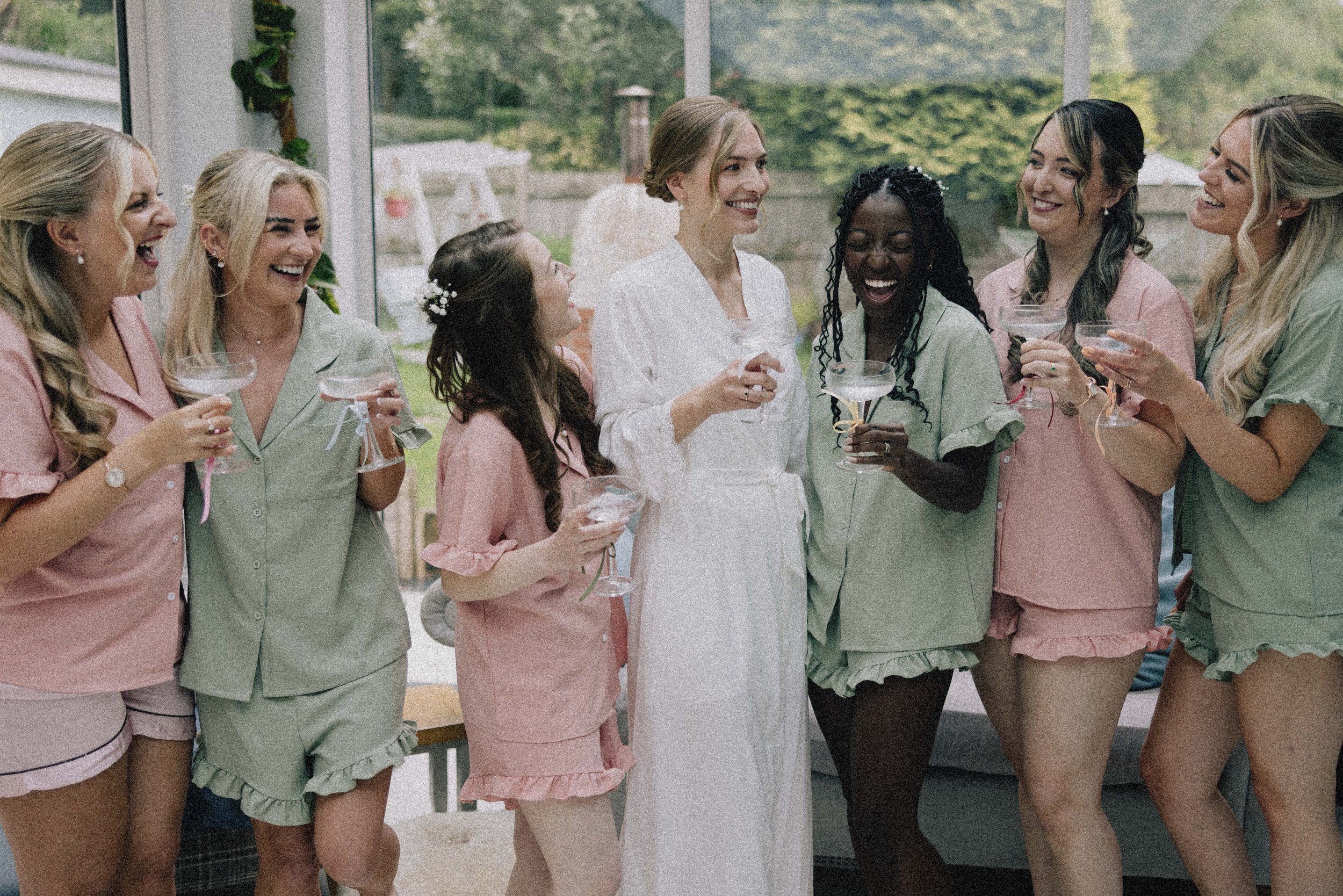 A group of women in pastel pajamas celebrating with champagne in a sunroom.