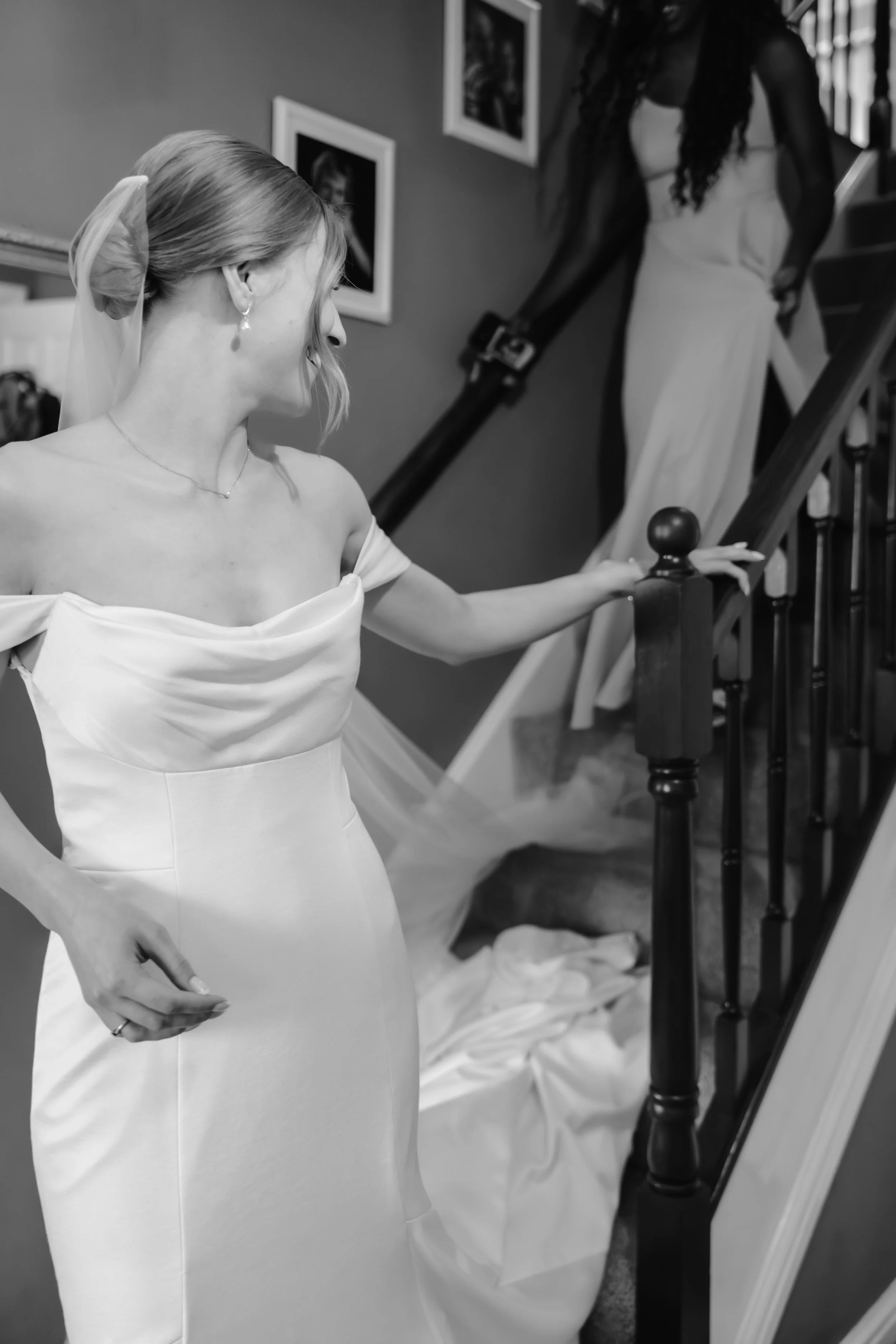 A bride in a wedding dress looking down at her dress while standing on a staircase, with a woman in the background helping on the stairs. wedding in telford