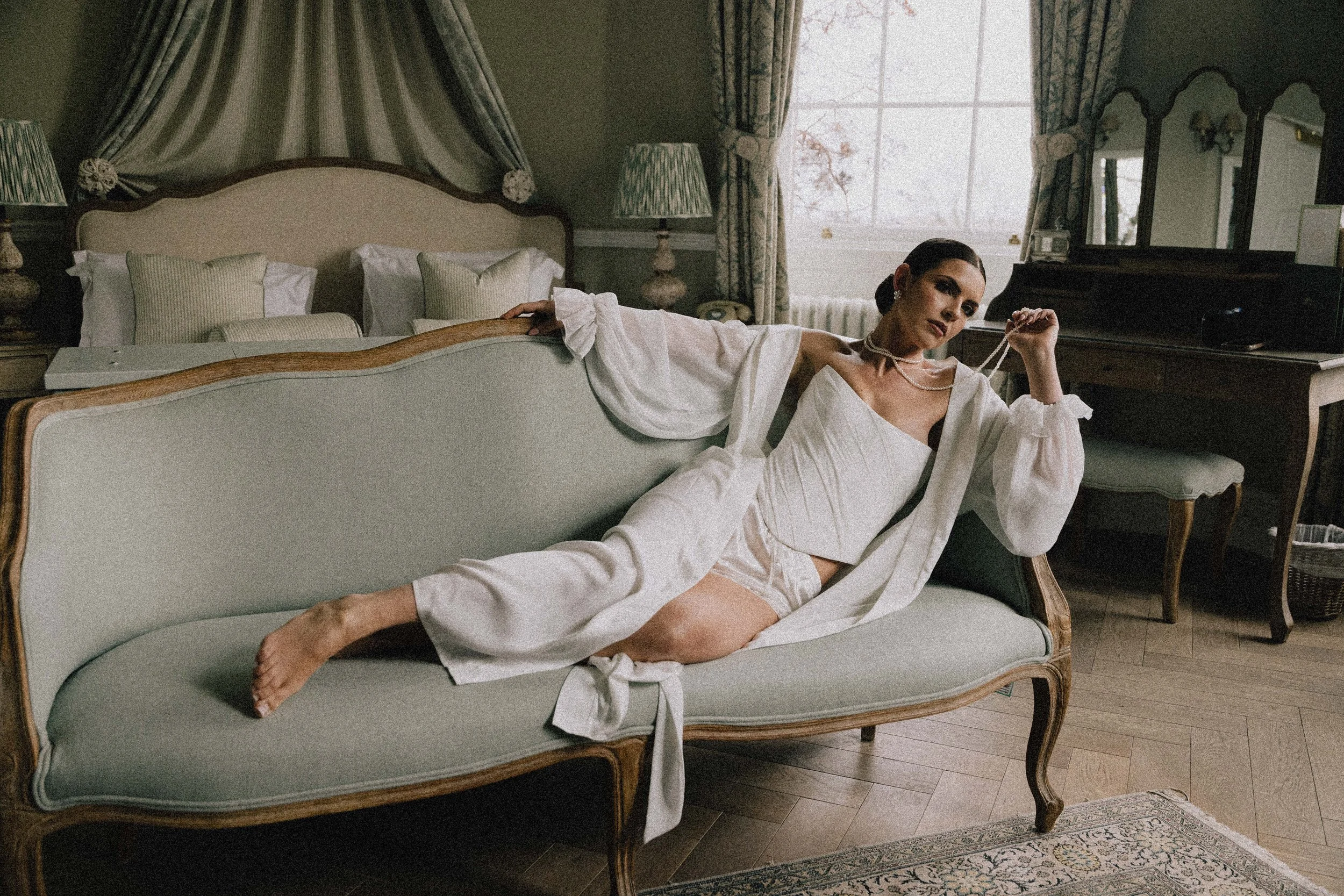 A woman lying on a vintage sofa in a bedroom, dressed in white clothing, with jewelry, and relaxed. 35mm film photography at middleton lodge 